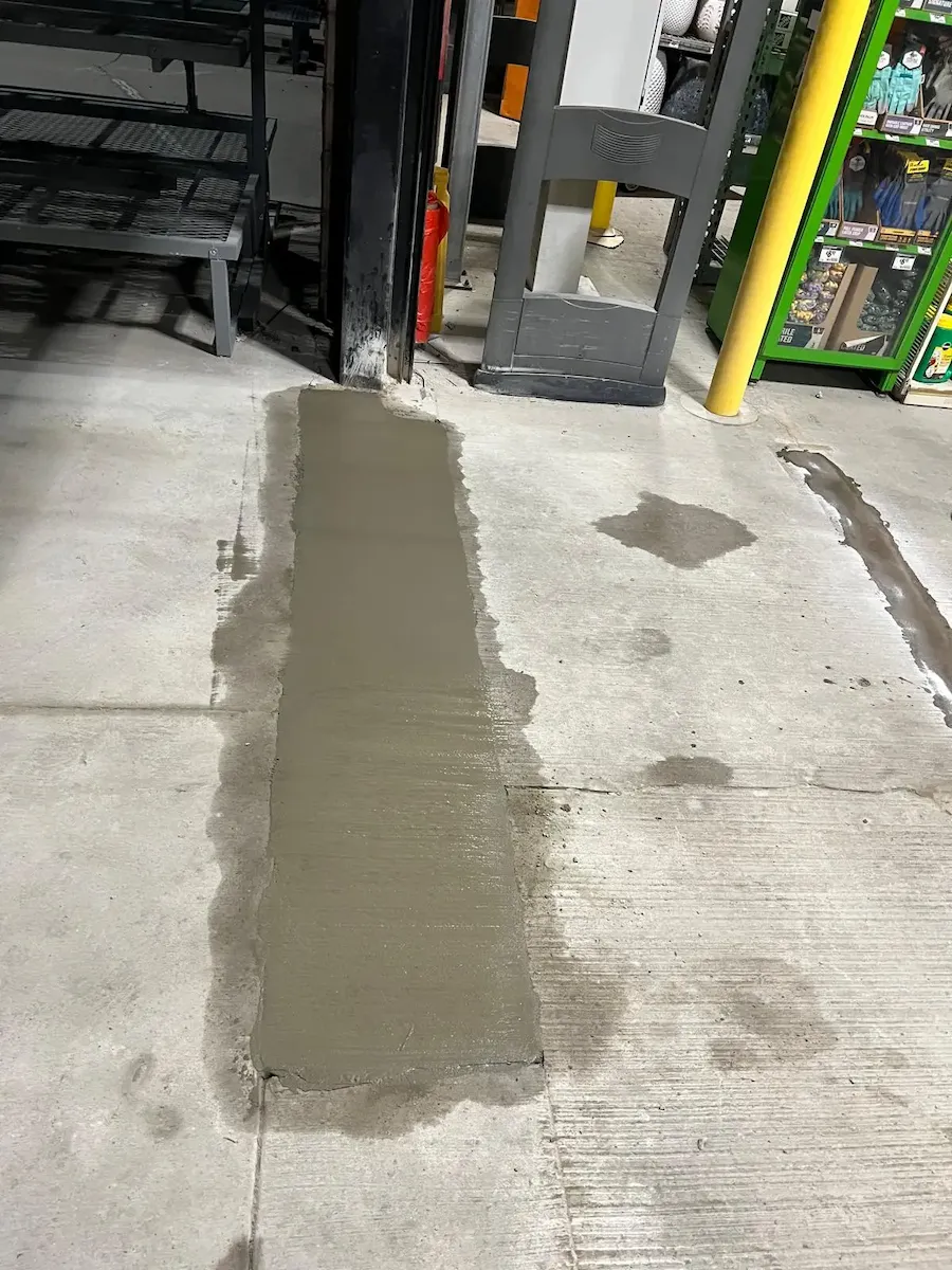 Initial pouring and leveling of fresh concrete in a commercial floor trench, repair mid-phase.